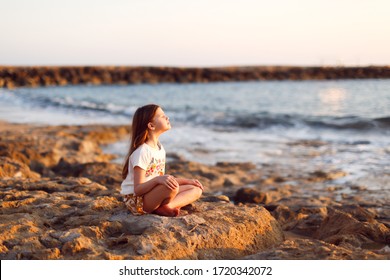 Girl child meditates sitting on stones at sea at sunset, concentration and yoga in children, calm and beauty - Powered by Shutterstock