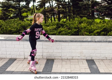 Girl child rollerblading in fall protection in the park. The child actively spends his free time, enthusiastically rollerblading. A girl in sportswear is engaged in roller skating. Free space for text