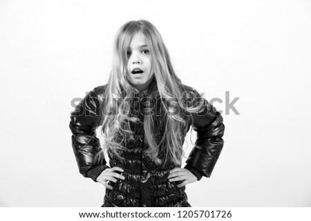 Girl child with surprised face and hands on hip with long blond hair in black jacket on orange background. Fashion, beauty, look, hairdresser concept