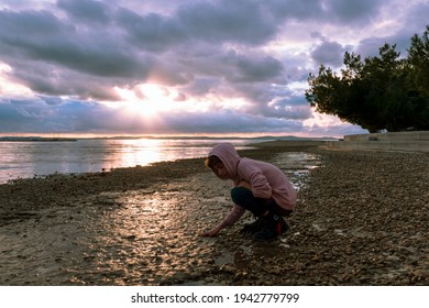 Girl Child Touching Wet Ground On The Beach At Sunset, Nin, Croatia. Selective Focus.