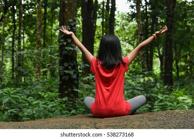 Girl Child Traveler Alone Sitting Relaxing On Rock In Calm Green Rain Forest Far From The City Away From Pollution, Kerala, India. Taking Deep Breath With Open Hands In Yoga Pose Inhale Fresh Air .