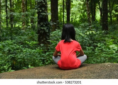 Girl Child Traveler Alone Sitting Relaxing On Rock In Calm Green Rain Forest Far From The City Away From Pollution, Kerala, India. Taking Deep Breath With Open Hands In Yoga Pose To Inhale Fresh Air .