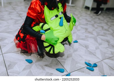 Girl Children's Animator In A Red Suit, Dress Holds A Green Soft Cat Toy At A Birthday Party, As A Gift To A Child. Festive Photo.