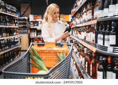 girl chooses wine in supermarket. girl reads labels on bottles of wine in supermarket.