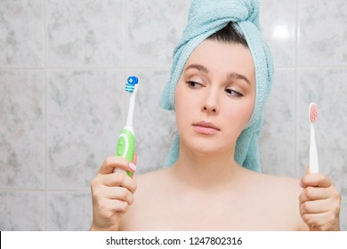 girl choosing an electric or ordinary toothbrush. Young woman holding toothbrushes in hands in the bathroom