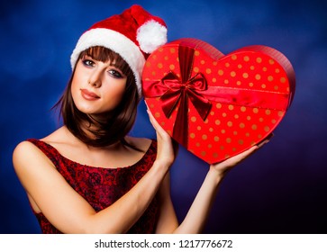 Girl in Christmas hat holding a gift box on violet background.
