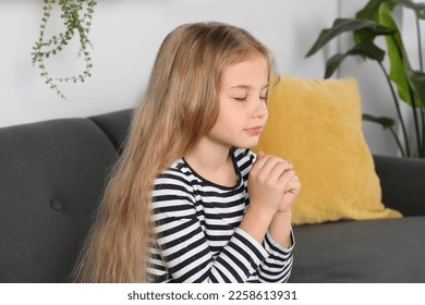 Girl with clasped hands praying on sofa at home - Shutterstock ID 2258613931