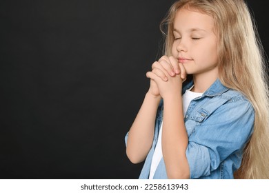 Girl with clasped hands praying on black background, space for text - Shutterstock ID 2258613943