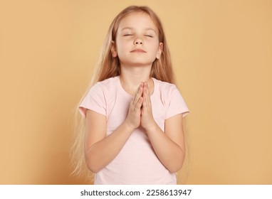 Girl with clasped hands praying on beige background - Shutterstock ID 2258613947