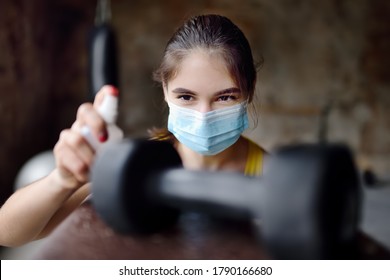 Girl cleaning of sport equipments of gym with  disinfecting spray. Woman making disinfection of dumbbells with sanitizer during epidemic. Protection and prevention from infection disease - Powered by Shutterstock