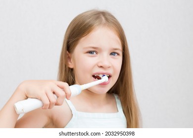 The girl cleans her teeth with an electric brush. Morning hygiene procedures. A beautiful smile. White teeth. - Powered by Shutterstock