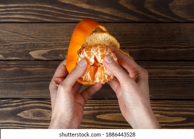 girl cleans a tangerine. view from above. hands clean the tangerine. wooden table. - Powered by Shutterstock