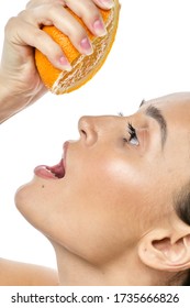 a girl with clear skin squeezes a fresh orange into her mouth on a white background