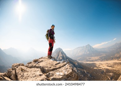 girl climber in a helmet and with a backpack stands on a mountain range against the backdrop of mountains and the sky. mountain climbing and hiking. - Powered by Shutterstock