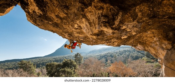 Girl climber on an overhanging rock. A sports woman climbs a rock against the backdrop of mountains. difficult movements in rock climbing. Difficult route in rock climbing.