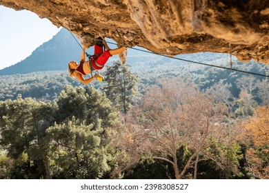 Girl climber on an overhanging rock. A sports woman climbs a rock against the backdrop of mountains. difficult movements in rock climbing. Difficult route in rock climbing.