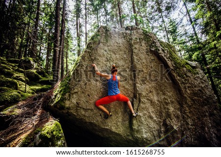 girl climbing hard boulder problem in forest. Sport climbing, bouldering.
