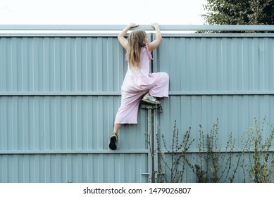 Girl climbing metal fence outdoor. Curious child on high white painted gates. Naughty kid playing outside, breaking rules. Childhood and youth concept. Restless teen entering private property - Shutterstock ID 1479026807
