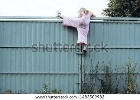 Girl climbing metal fence outdoor. Curious child on high white painted gates. Naughty kid playing outside, breaking rules. Childhood and youth concept. Restless teen entering private property