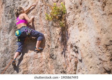 A girl climbs a rock. The athlete trains in nature. Woman overcomes difficult climbing route. Strong climber. Extreme hobby. Rock climbing in Turkey.