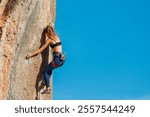 The girl climbs the rock. The climber is training to climb the rock. A strong athlete overcomes a difficult climbing route. Extreme hobby. A woman goes in for sports in nature. 
