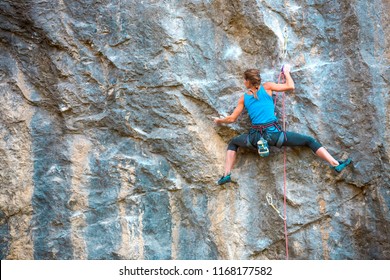 The Girl Climbs The Rock. The Climber Is Training To Climb The Rock. A Strong Athlete Overcomes A Difficult Climbing Route. Extreme Hobby. A Woman Goes In For Sports In Nature. Natural Rocky Terrain.