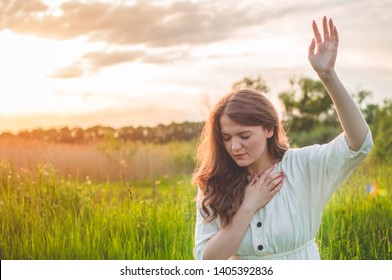 Girl closed her eyes, praying in a field during beautiful sunset. Hands folded in prayer concept for faith, spirituality and religion. Peace, hope, dreams concept