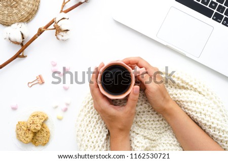 girl with a coffee in her hands. Oatmeal cookies, laptop, and sweets. A good start to a winter day. Cotton flowers decorate the table. Autumn or Winter concept. Flat lay, top view