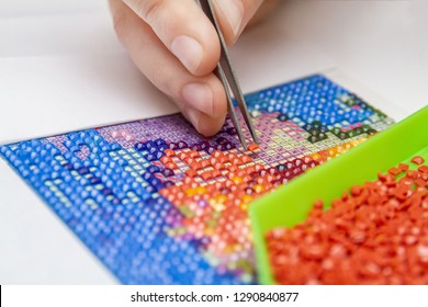 Girl collect diamond painting. Diamond embroidery with a tweezers. Acrylic rhinestones. Closeup, selective focus