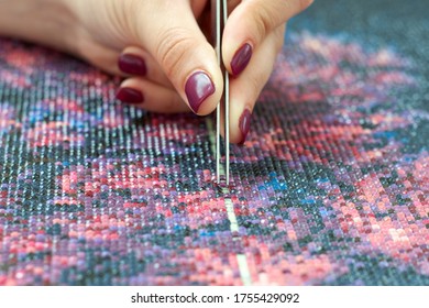 Girl collect diamond painting. Diamond embroidery with a tweezers. Acrylic rhinestones. Closeup, selective focus