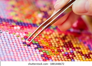 Girl collect diamond painting. Diamond embroidery with a tweezers. Acrylic rhinestones. Close-up, selective focus