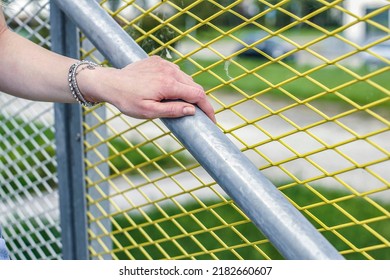 Girl comes downstairs holds onto handrail against net fence wearing a bracelet