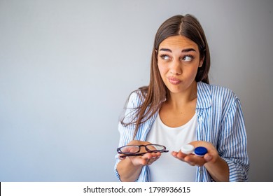 Girl Comparing Contacts To Eyeglasses For Vision Correction. Woman Choosing Between Contact Lenses And Glasses In Optic Store. Woman Thinking To Choose Contact Lenses Over Eyeglasses