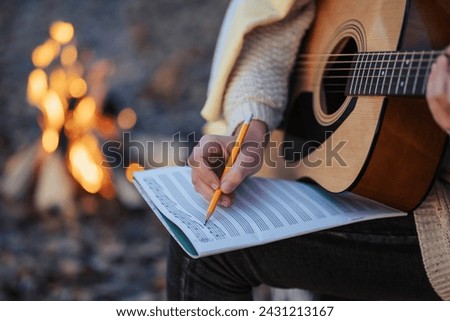 Girl composer playing the guitar composing new song outdoors near bonfire. Playing the guitar in autumn park in the evening, making new composition