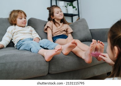 Girl conducting tickling competition between siblings sitting on a couch using a feather. Their faces blurred, focus on feet.