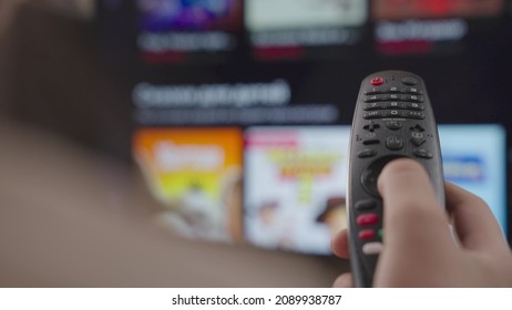 Girl Controls The TV Remote Control In Room At Home, Rest On Weekend, Remote Control Of A Modern Smart TV, Control TV And Movie Channels, Close-up, Blurred Display Screen, Smart Page Scrolling Device