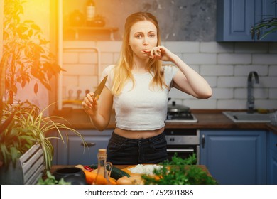 The girl is cooking and cut herself in the kitchen. A woman prepares a salad of fresh vegetables and herbs. Healthy eating on a diet. Knife in the hands of a girl. Cut finger. Injury while cooking.