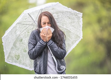 Girl Coughing Into A Napking Having A Flu, Walking Outside On A Rainy Day With An Umbrella.