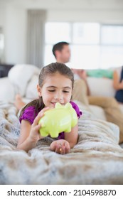 Girl Counting Change In Piggy Bank On Sofa In Living Room