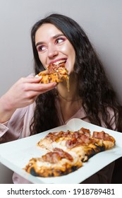 Girl Courier Eating Pinsa Pizza Romana Gourmet Italian Cuisine On Grey Background. Holding Scrocchiarella Traditional Dish. Food Delivery From Pizzeria. Pinsa With Meat, Arugula, Olives, Cheese.