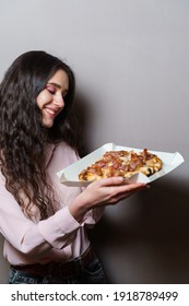 Girl courier with pinsa romana gourmet italian cuisine on grey background. Holding scrocchiarella traditional dish. Food delivery from pizzeria. Pinsa with meat, arugula, olives, cheese. - Shutterstock ID 1918789499