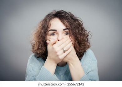 girl covering her mouth with her hands, scared on a gray background - Shutterstock ID 255672142