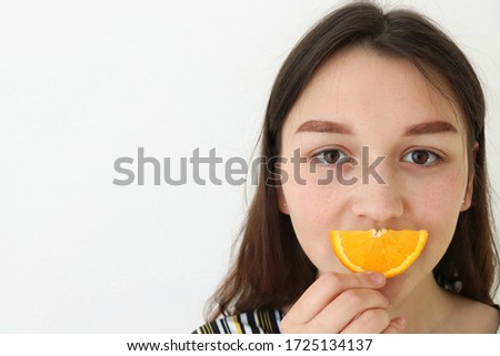 The girl covers part of her face with an orange. The summer mood. On white background. Space for your text