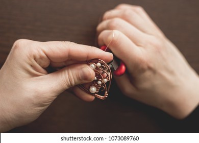 Girl Craftsman Making Copper Wire Wrapped Jewelry Heart Pendant With Pearls Close Up Top View. Female Hands Holding Adornment Jewelery Handmade Art Product. Accessories Bijouterie