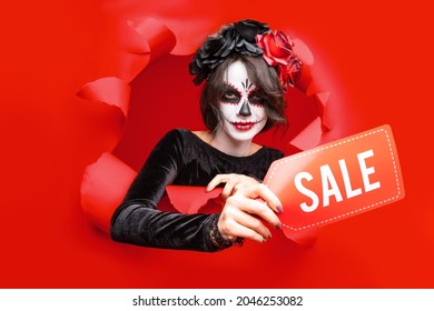Girl with creative sugar skull makeup with wreath of flowers on head,  isolated red paper hole background. Concept Dia De Los Muertos poster for Halloween party or La Calavera Catrina. Holiday sale.