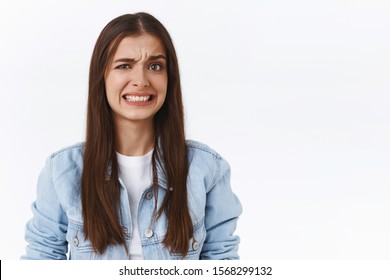 Girl cringe as seeing something embarrassing and bothering. Woman make uncomfortable smile and squinting feeling worried and displeased, see bothering bad situation, standing white background