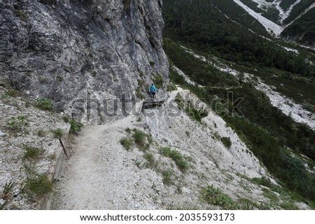 A girl crosses a wooden bridge on a rough and dangerous path while trekking in the Italian Alps.