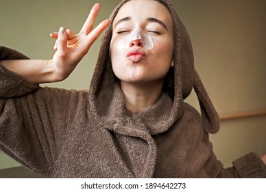 Girl In A Cute Bathrobe, Dressing Gown With Bunny Ears. Woman Has Fun With A Facial Mask.A Woman Applies Cleansing, Moisturizing Strips To Her Nose,  Mask From Blackheads.