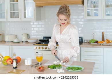 Girl cuts fruit salad with strawberries on cutting board with knife. Concept cooking sliced fresh fruits Beautiful woman with makeup and hairstyle in light dress enjoys morning and preparing breakfast