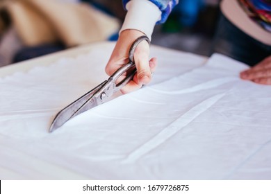 Girl cuts a white cloth with scissors on the table